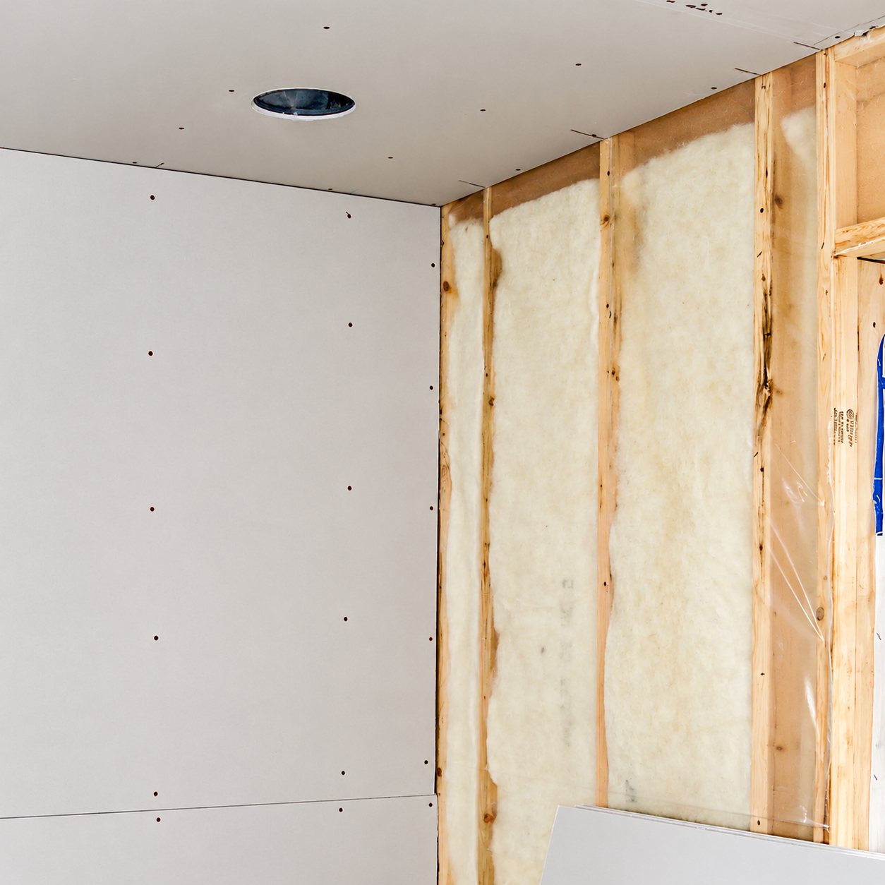 Angle d'une pièce en chantier où un mur est recouvert de plaques de plâtre et l'autre montre l'ossature en bois remplie d'isolant.