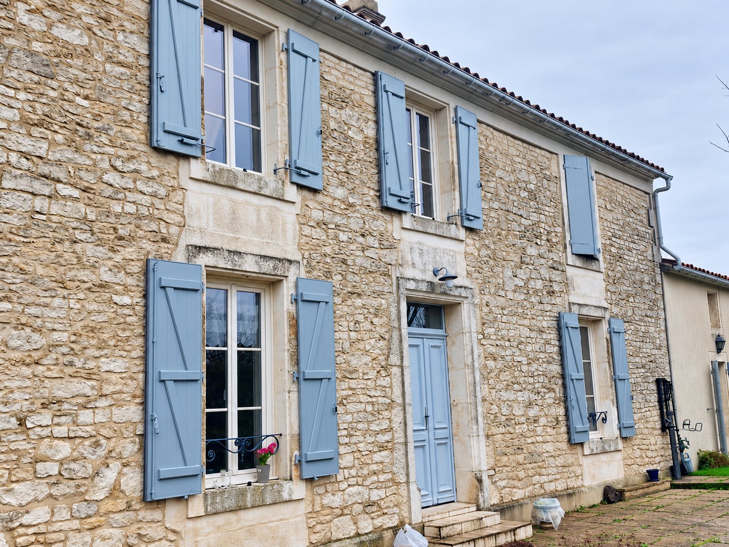 Façade d'une maison ancienne en pierres apparentes avec des volets en bois peints en bleu-gris et une porte d'entrée assortie.
