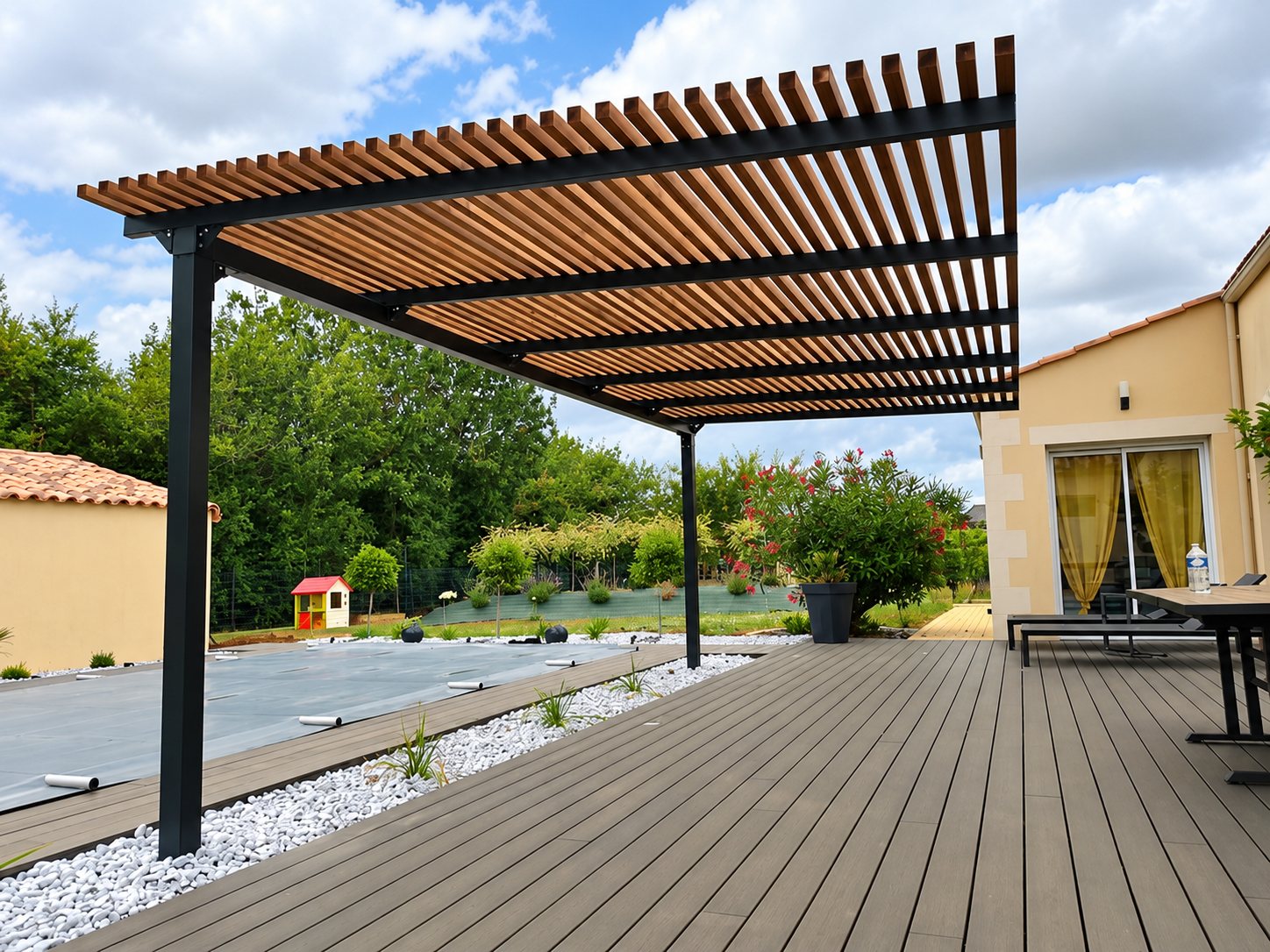 Une pergola en métal sombre à lames de bois couvre une terrasse en composite gris, avec une piscine bâchée et un jardin en arrière-plan.