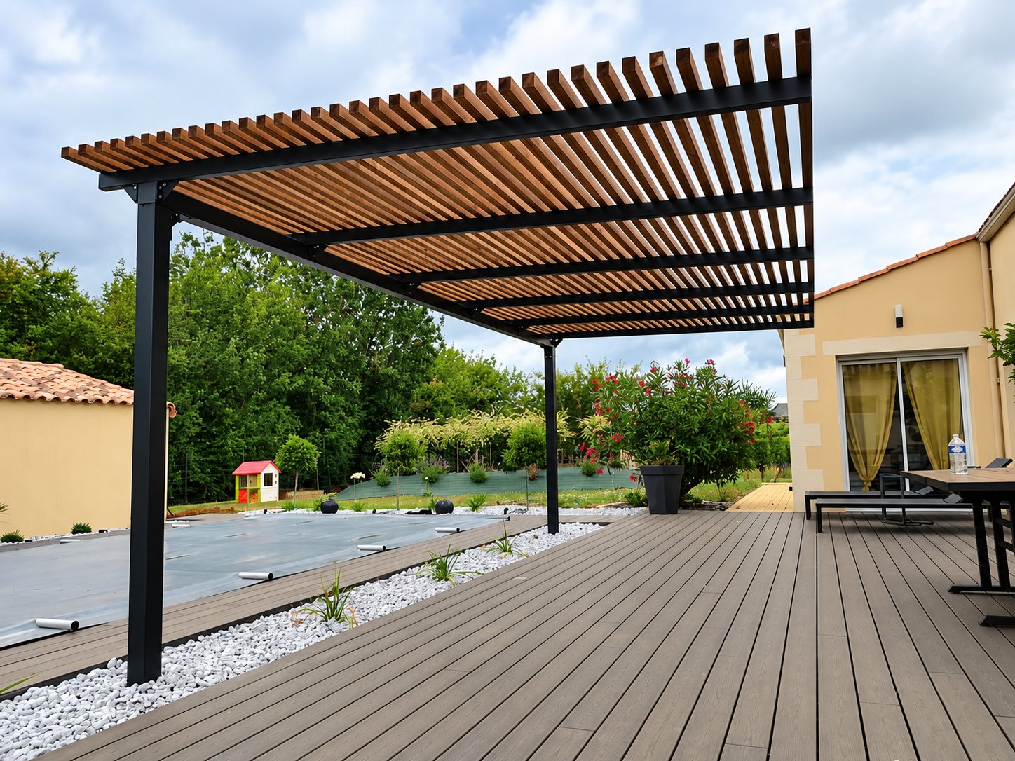 Une pergola à structure métallique sombre et lames de bois couvre une terrasse en composite grise, avec une piscine bâchée et un jardin en arrière-plan.