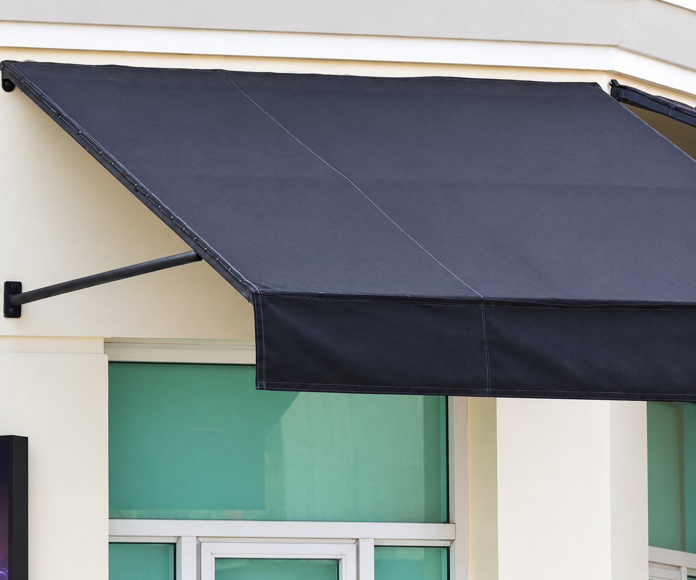 Un store banne fixe en toile gris anthracite, soutenu par un bras métallique, protège une fenêtre sur une façade beige.